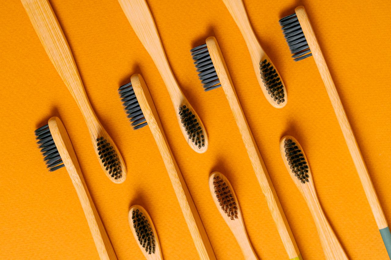 Collection of wooden toothbrushes with natural bristles on an orange surface.