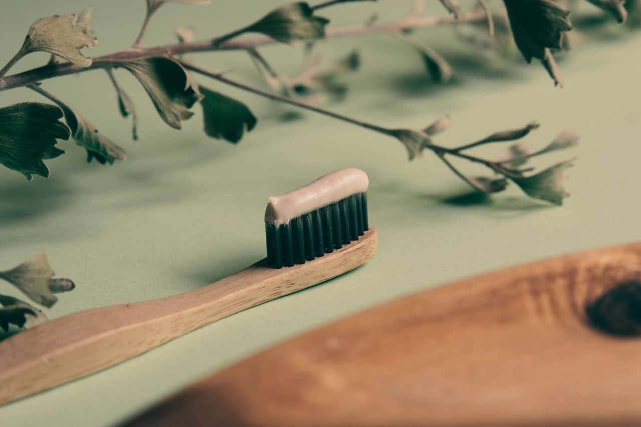 Wooden toothbrush with toothpaste on greenery background, promoting eco-friendly dental hygiene.
